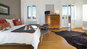 Een slaapkamer met een bed, een kaptafel en uitzicht op de stad door open deuren.