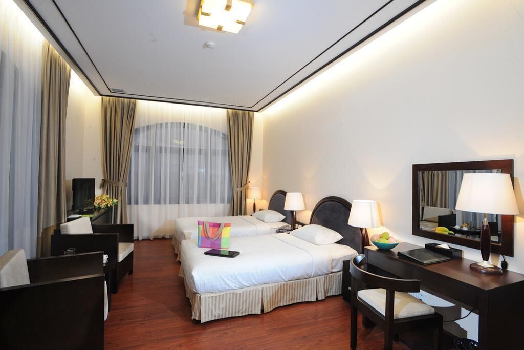 A hotel room with two beds, a desk, a chair, a TV, and a large window with curtains.
