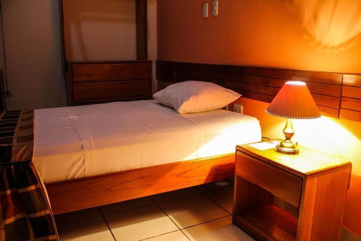 Cama bem arrumada com cabeceira de madeira e mesa de cabeceira com abajur.