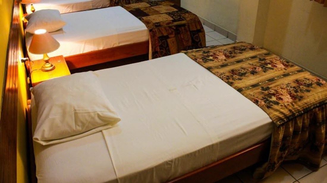 A room with two beds, each with a different style of bedding and a lamp on the left side.