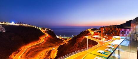 A coastal road with a winding path leading to a beach area with sun loungers and a pool.