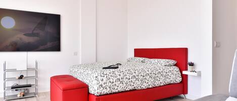 A modern bedroom with a red bed, a white wall, and a painting of a sailboat.