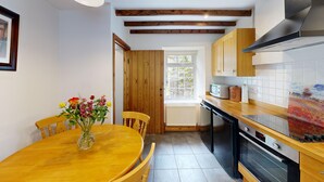A compact kitchen with wooden cabinets, a built-in oven, and a dining area with a wooden table and chairs. - 19th century stable with four poster, river views and free WiFi (SWANSEA)