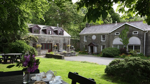 A stone building with a garden patio, a wooden table with tea set, and a bench. - 19th century stable with four poster, river views and free WiFi (SWANSEA)