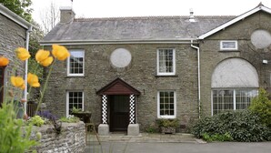 A stone building with a central entrance, a small porch, and a large window on the right. - 19th century stable with four poster, river views and free WiFi (SWANSEA)