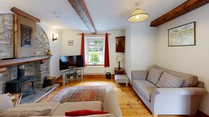 A cozy living room with a stone fireplace, a television, a sofa, and a wooden floor. - 19th century stable with four poster, river views and free WiFi (SWANSEA)
