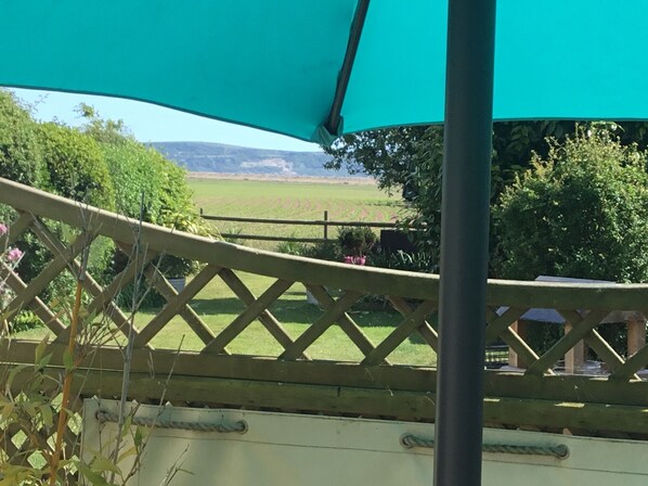 A view from a balcony with a wooden lattice railing, a green umbrella, and a landscape of fields and trees in the background. - Beaches Studio is in a Fabulous Location with Views to the Shingle Bank and Iow (Milford on Sea)