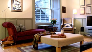 Un salon chaleureux avec un canapé rouge, un plaid et une table basse en bois sur laquelle se trouvent un plateau de verres et une bouteille.