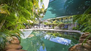 Zona de piscina con sillones reclinables, una piscina cristalina y vegetación tropical circundante.