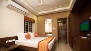 Quarto de hotel com cama, mesa de cabeceira, ar condicionado, televisão e guarda-roupa de madeira.