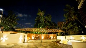 Uma área de estar ao ar livre com pérgola, assentos e iluminação ambiente.