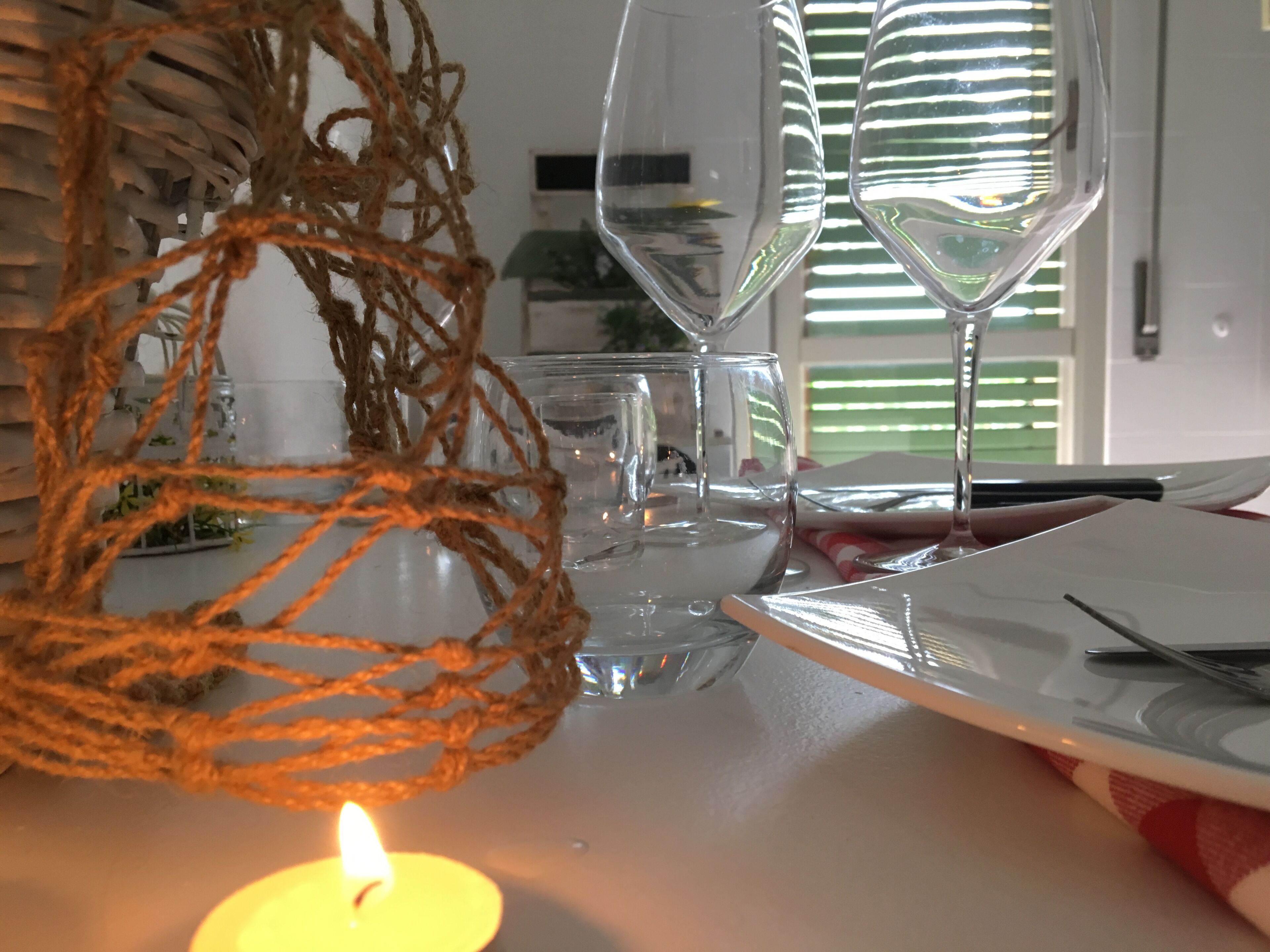 A table with two clear wine glasses, a lit candle, and a woven decorative item.