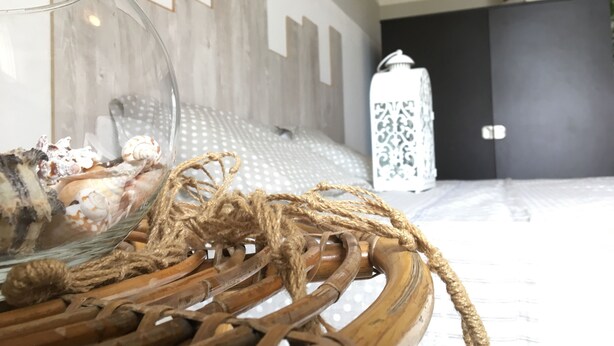 A wicker basket with a glass container and rope, a polka-dotted pillow, and a patterned lantern in a room with wooden paneling and a dark door. - The moon and the bonfire IT009024C2SF9H64V7 (Ceriale)