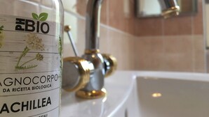 A bathroom with a white sink, a gold faucet, and a bottle labeled "PH BIO" with "ACHILLEA" on it. - The moon and the bonfire IT009024C2SF9H64V7 (Ceriale)