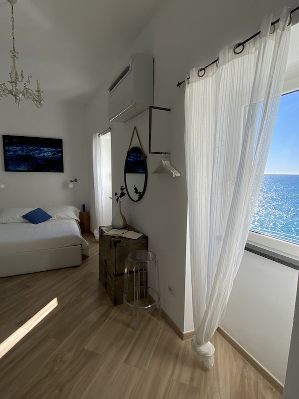 A modern bedroom with a bed, a large window with curtains, a chandelier, and a wall-mounted mirror.
