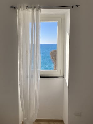 A room with a window overlooking a rocky coastline.