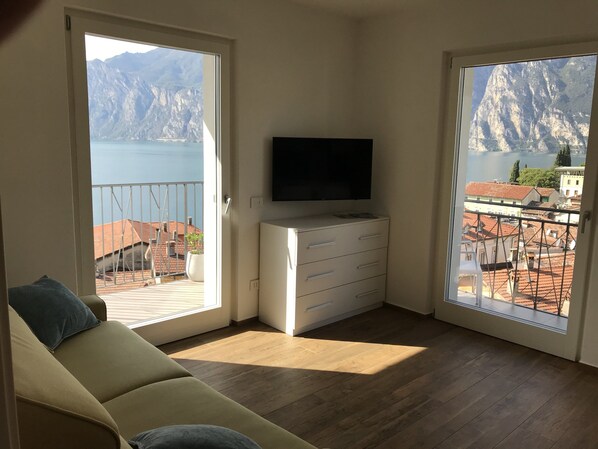 Una habitación con sofá, televisor en una cómoda y amplios ventanales con vistas a la montaña y al lago.