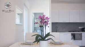 Eine moderne Küche mit weißen Schränken, einem eingebauten Backofen und einem Gasherd. Ein Esstisch ist gedeckt mit weißen Tellern, klaren Gläsern und einer Vase mit violetten Blumen.