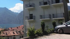 Ein mehrstöckiges Gebäude mit Balkonen, ein Auto davor und eine Bergkulisse im Hintergrund.