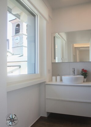 Une salle de bain moderne avec une grande fenêtre, un lavabo blanc et un miroir.