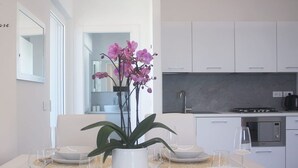 A modern kitchen with white cabinets, a built-in oven, and a gas stove. There is a dining table set with white plates, clear glasses, and a vase with purple flowers.