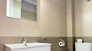 Kylpyhuoneessa on valkoinen pesuallas, peili, wc-istuin ja seinällä wc-paperirulla.