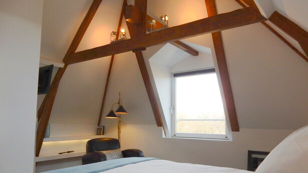 A bedroom with a sloped ceiling, a bed, a desk with a chair, and a window.