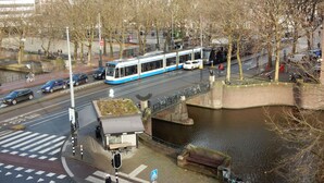 A tram crossing a bridge over a river, with a café and benches nearby.