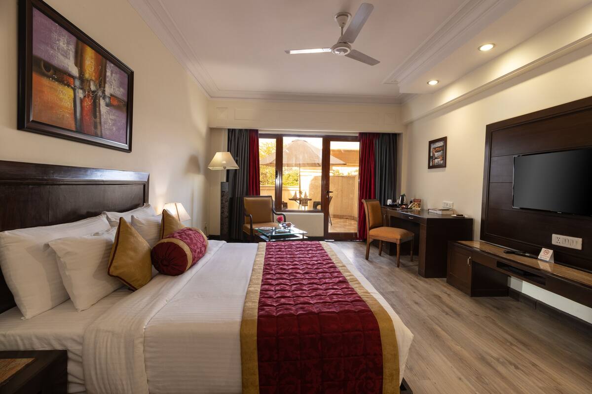 A hotel room with a large bed, a desk, a television, and a view of the outdoors.