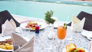 Una tavola da pranzo con diversi piatti, bevande e una piscina sullo sfondo.