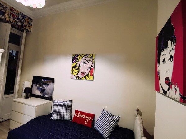 A bedroom with a bed, a nightstand, a lamp, and two paintings on the wall.