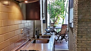 Una cucina moderna con piano cottura a gas, lavello in acciaio inossidabile e schienale in mattoni. Si intravede un'area pranzo con tavolo e sedie attraverso una porta aperta.