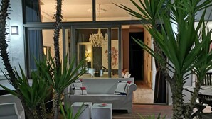 Zona relax esterna moderna con pavimento in legno, divani bianchi e fioriere con piante alte.