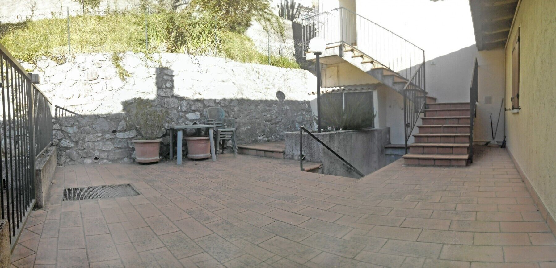 Ein Innenhof mit einer Steinmauer, einem Metallgeländer und einer Treppe, die zu einer oberen Ebene führt.