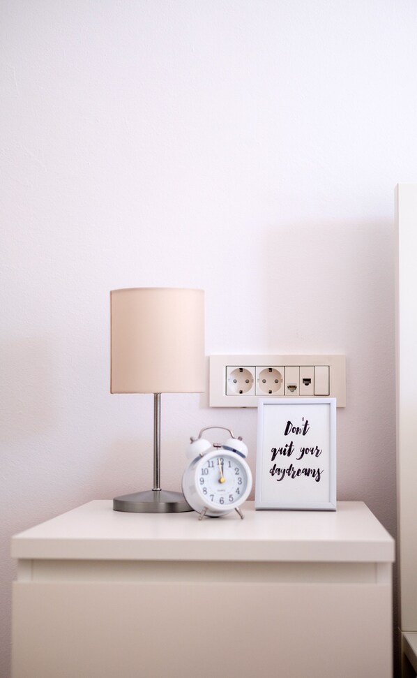 A bedside table with a lamp, an alarm clock, and a motivational quote sign.