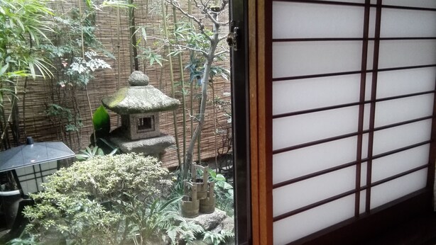 Ein traditioneller japanischer Garten mit Steinleuchte, Bambus und Blick durch einen Shoji-Bildschirm.