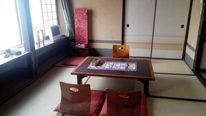 Ein Raum mit Tatami-Matten, einem niedrigen Tisch, Kissen und einer traditionellen japanischen Schiebetür.