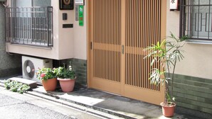 Ein traditionelles japanisches Gebäude mit Holztür, Topfpflanzen und einem Schild.