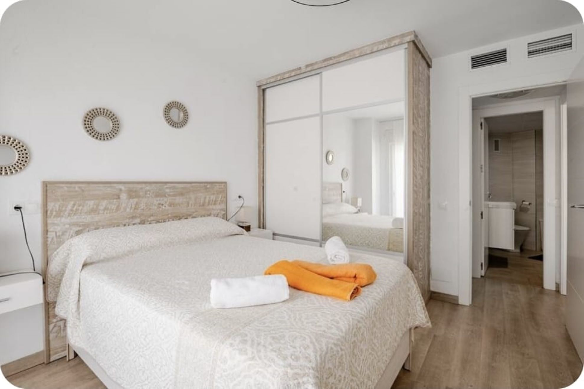 A bedroom with a bed, a wardrobe, a mirror, and a bathroom visible through an open door.