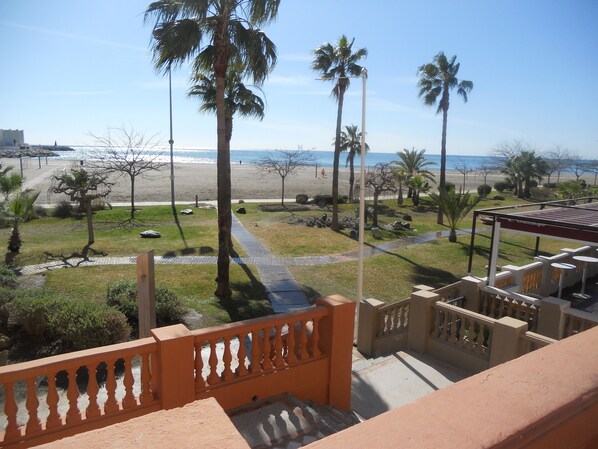 A balcony with a view of a beach, palm trees, and a clear sky.