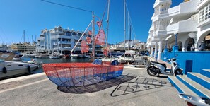 Un puerto deportivo con barcos amarrados, una moto y un edificio de arquitectura blanca y azul.