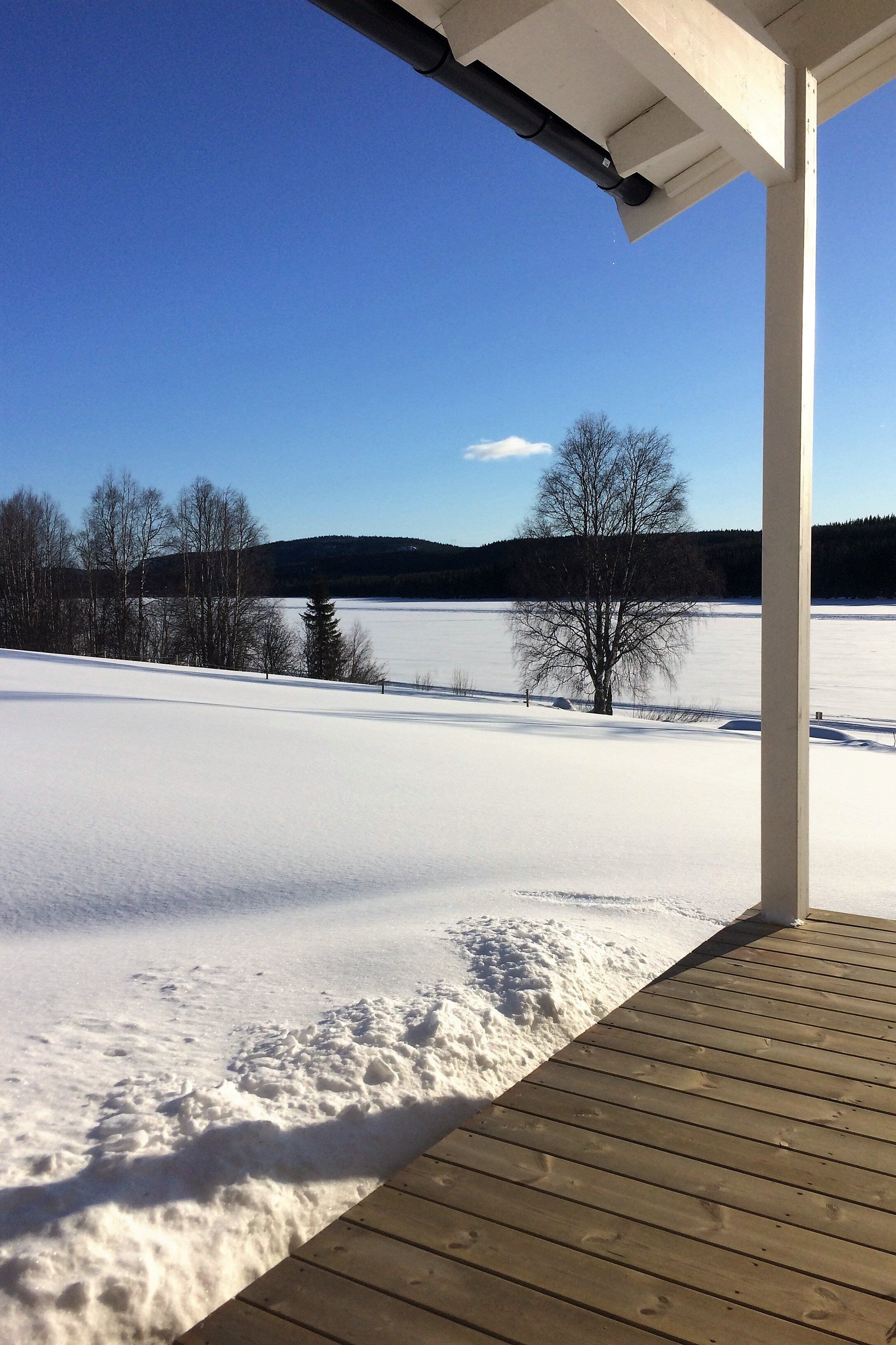 A wooden deck overlooking a snow-covered field with a clear blue sky.