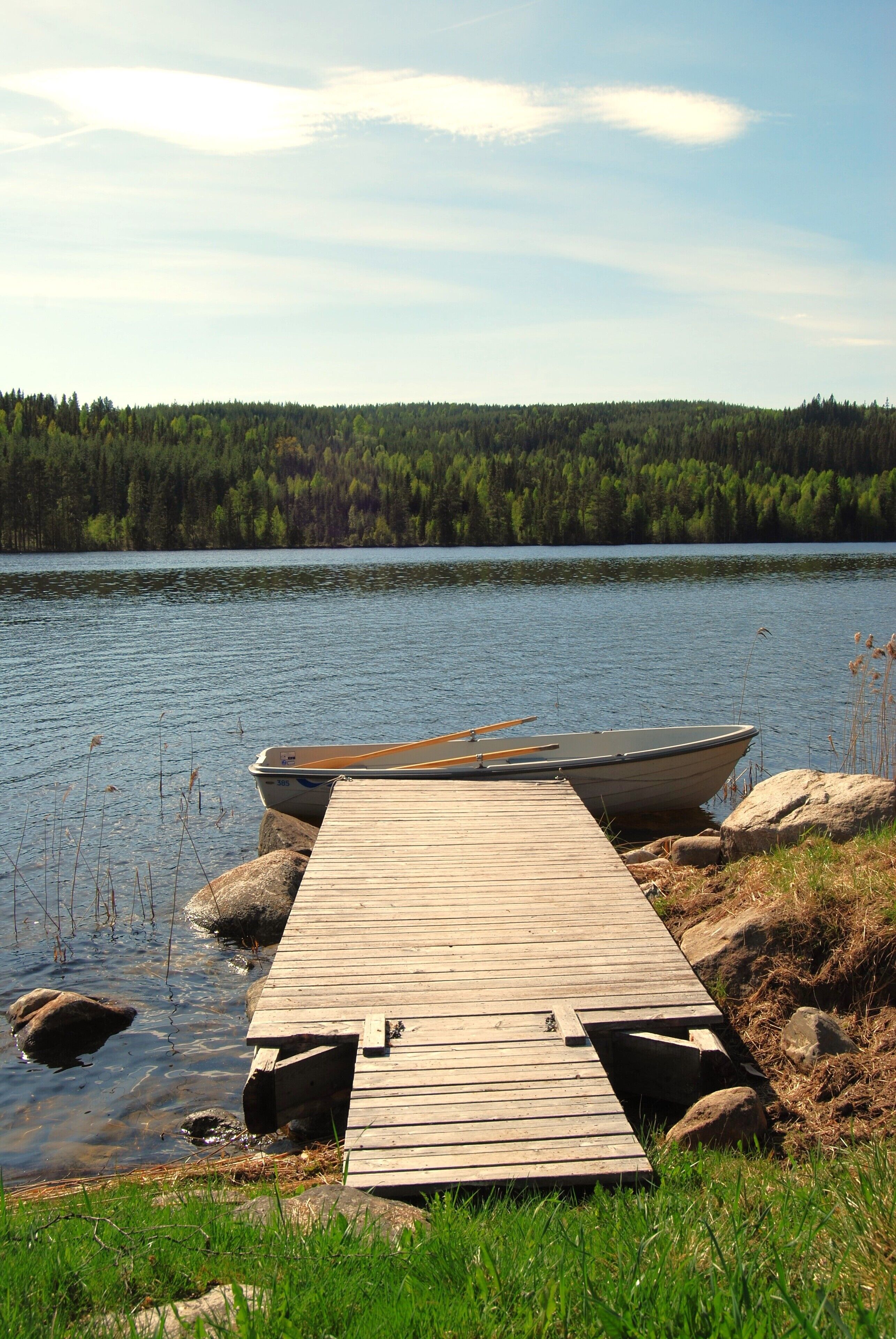 A wooden dock extending into a calm lake, surrounded by rocks and grass.
