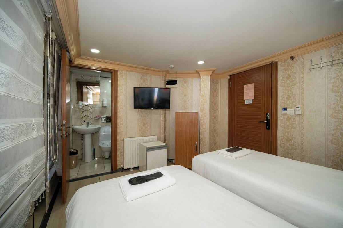 A hotel room with two beds, a television, a bathroom with a sink and toilet, and a mirror.