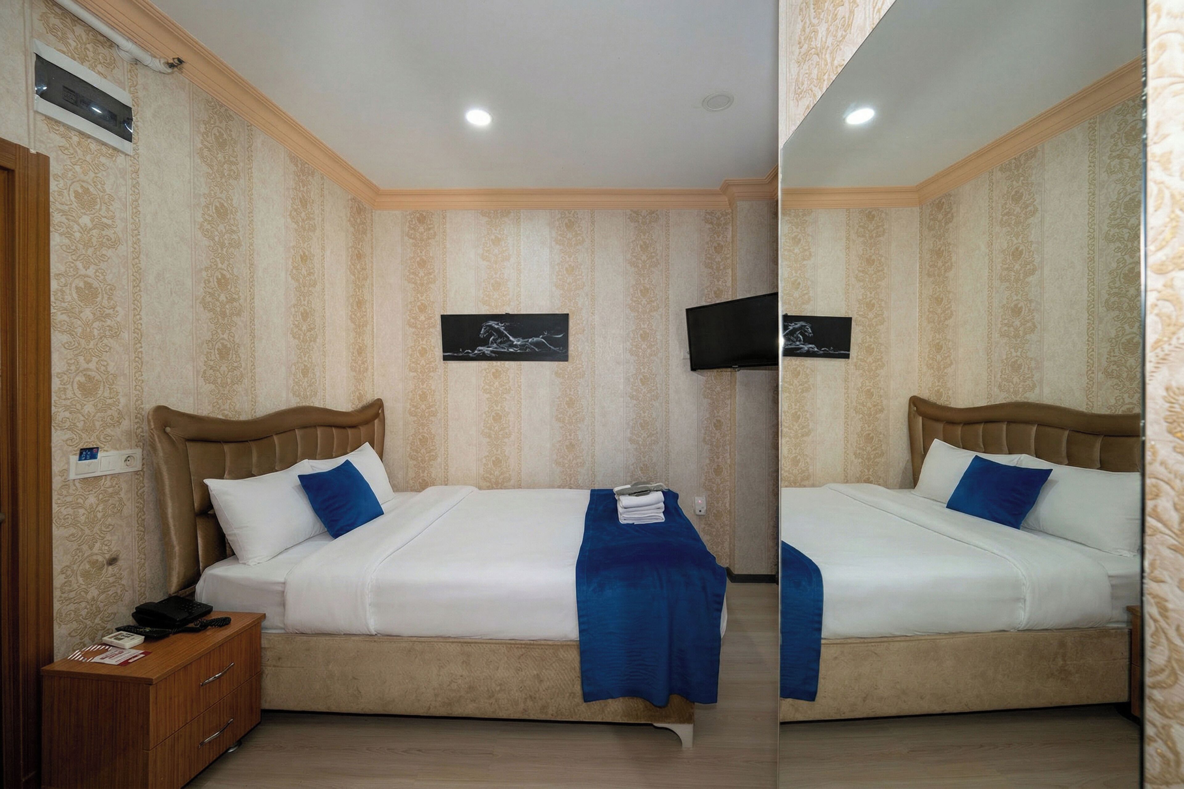 A double bed with a blue throw blanket, a bedside table with a phone, and a TV mounted on the wall.