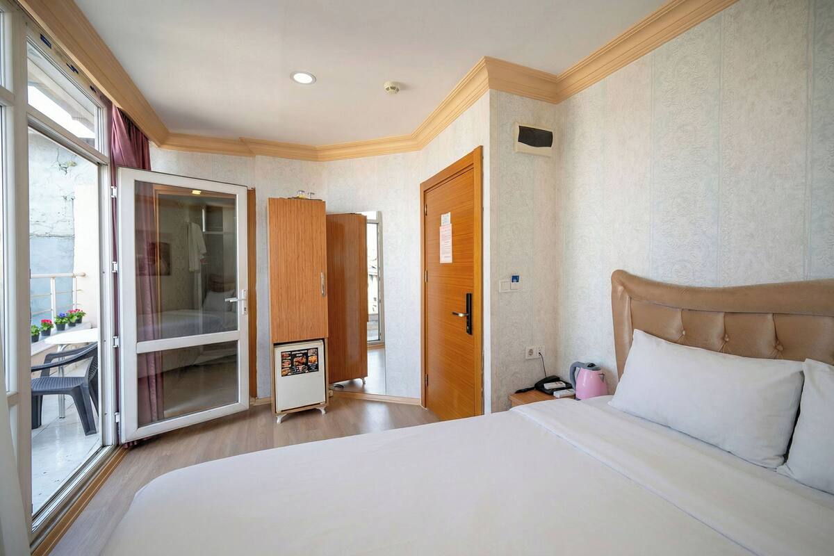 A hotel room with a bed, a wardrobe, a desk, and a sliding glass door leading to an outdoor area.