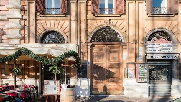 Un immeuble avec un commerce au rez-de-chaussée, une grande porte en bois et une enseigne indiquant qu’il s’agit d’un magasin de photos et de souvenirs.