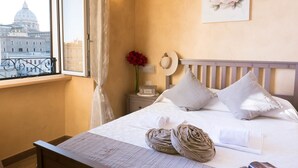 Une chambre à coucher avec un lit, une table de chevet, une fenêtre donnant sur un immeuble et un mur orné d’un tableau représentant des fleurs.