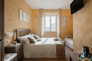 Un dormitorio con cama, mesitas de noche, televisor y ventana con cortinas.