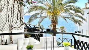 Eine Terrasse mit weißen Sitzkissen, einem Glastisch und einem Blumentopf.